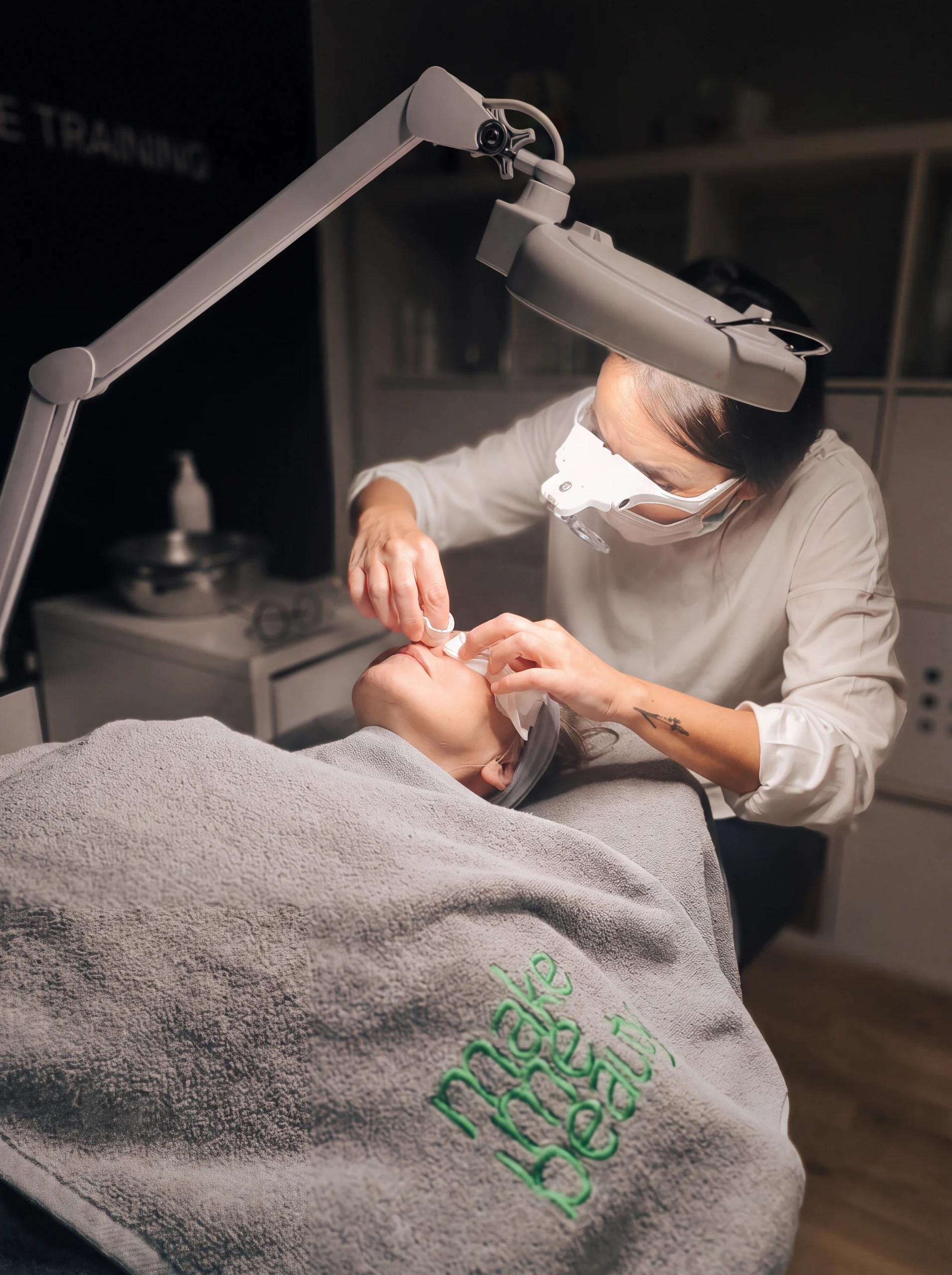 Kosmetikerin behandelt das Gesicht einer Kundin unter einer Lupenleuchte im MakeMeBeauty-Studio.